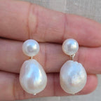 Pearl earrings held between fingers against a neutral background