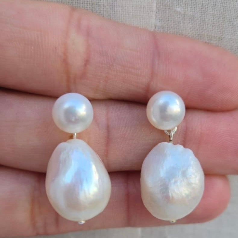 Pearl earrings held between fingers against a neutral background