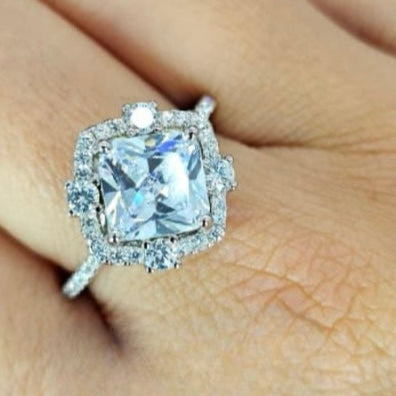 A sterling silver ring with a large central cubic zirconia surrounded by smaller cubic zirconia stones, displayed on a person's hand.