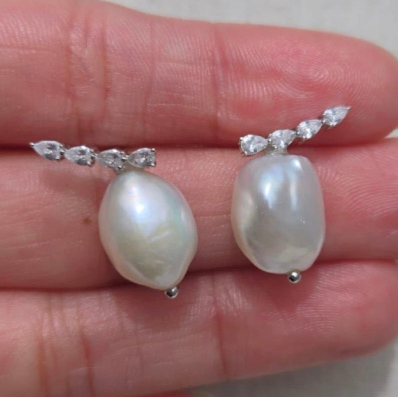 Pearl earrings with silver clasps held between fingers on a neutral background