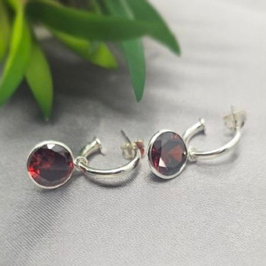 A pair of sterling silver earrings with red cubic zirconia crystal drops placed on a linen surface.