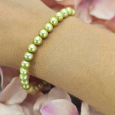 A green freshwater pearl bracelet displayed on a person's wrist with a background of pink flowers.