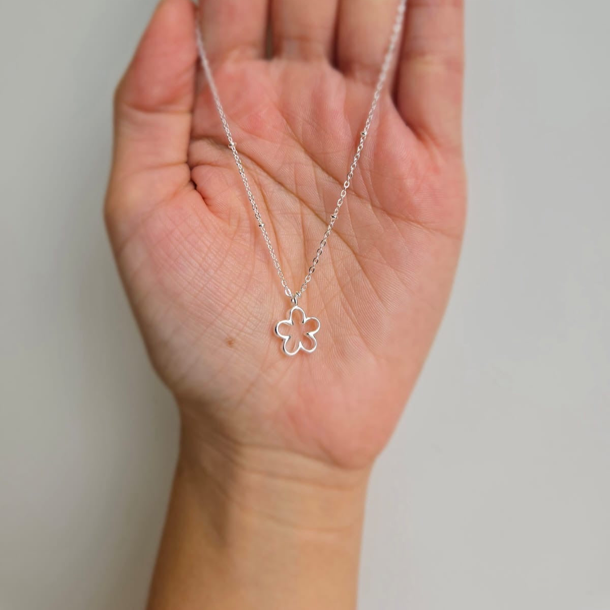 A hand holding a sterling silver necklace with a small open flower pendant.