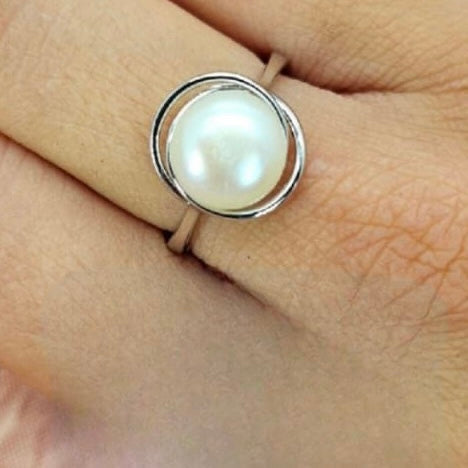 A sterling silver ring with a large freshwater pearl set in a wave-like mounting, displayed on a person's finger.
