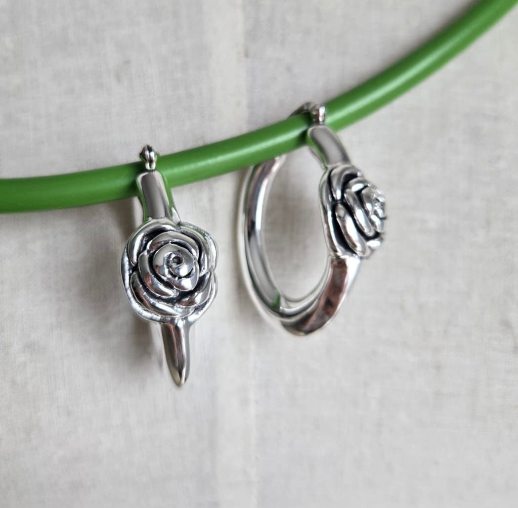 Silver hoop earrings with rose designs on a green branch against a light background