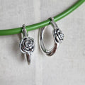 Silver hoop earrings with rose designs on a green branch against a light background