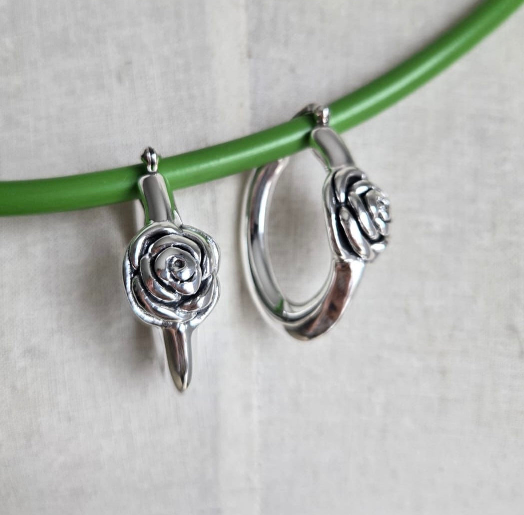 Silver hoop earrings with rose designs on a green branch against a light background