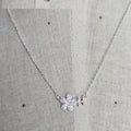 Silver necklace with a floral pendant on a textured gray background