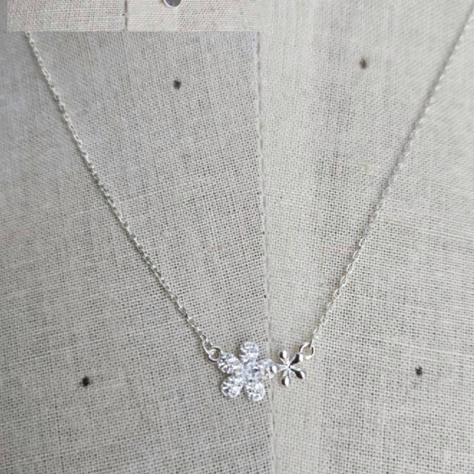 Silver necklace with a floral pendant on a textured gray background
