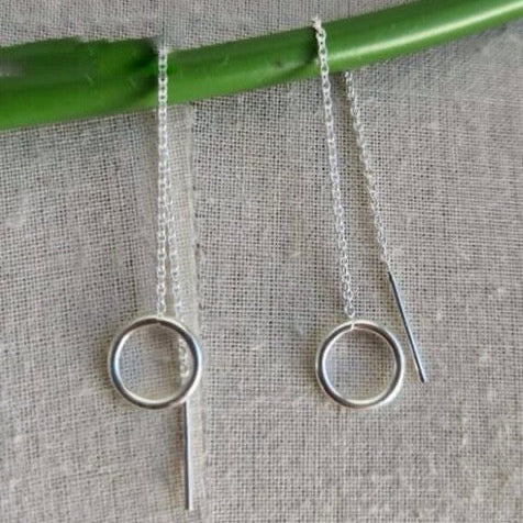 Silver circle earrings hanging from a green stick on a textured fabric background