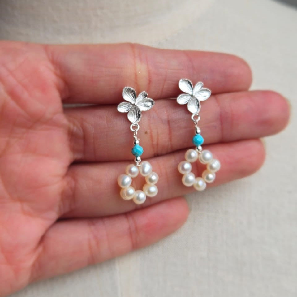 Silver earrings with floral and pearl designs held in a hand against a neutral background