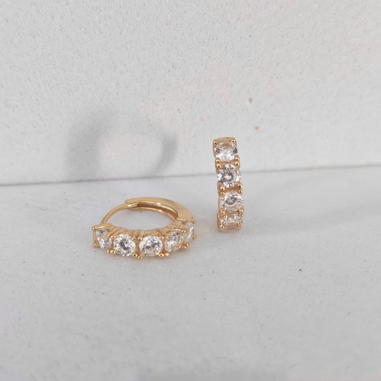 Pair of rose gold hoop earrings with clear gemstones on a light gray background