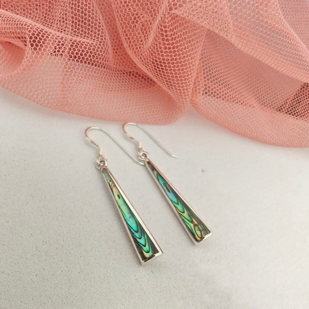 Green and gold earrings on a white surface with pink fabric in the background