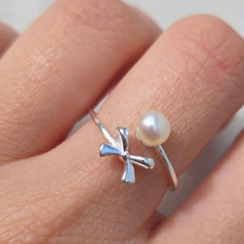 Silver ring with a pearl on a finger against a neutral background