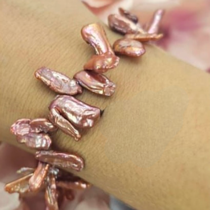 A bracelet featuring uneven freshwater pearls in pink and silver colors, strung on an elastic band.