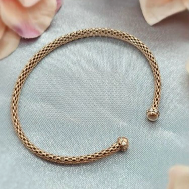 A rose gold plated sterling silver mesh bracelet lying on a surface with a floral pattern.