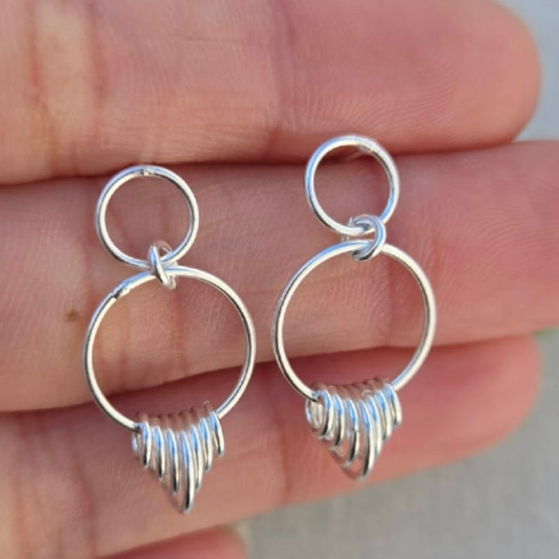 Silver hoop earrings held between fingers against a neutral background