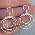 Silver hoop earrings held between fingers against a neutral background