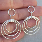 Silver hoop earrings held between fingers against a neutral background