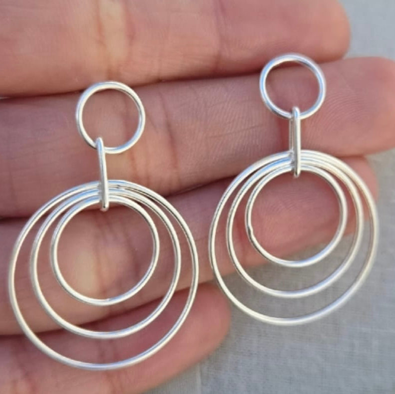 Silver hoop earrings held between fingers against a neutral background