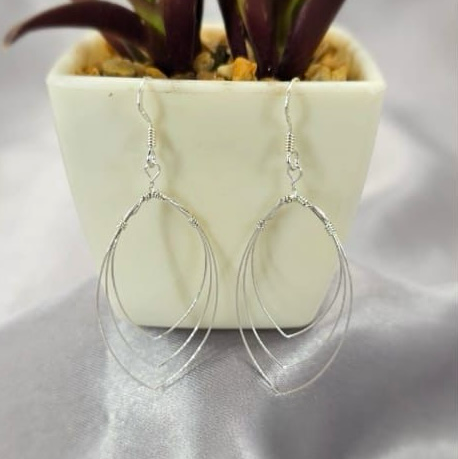 Two silver drop earrings displayed in front of a potted plant with purple leaves.