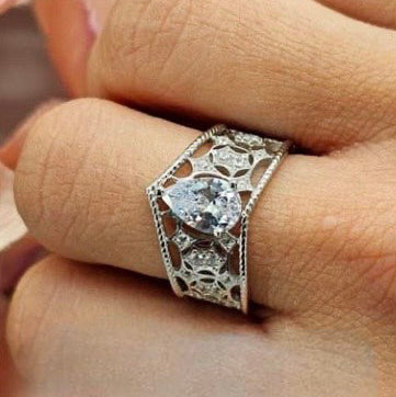 A V-shaped silver ring encrusted with cubic zirconia filigree, displayed on a person's finger.