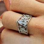 A V-shaped silver ring encrusted with cubic zirconia filigree, displayed on a person's finger.