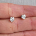 Heart-shaped silver earrings with clear gemstones on a hand.