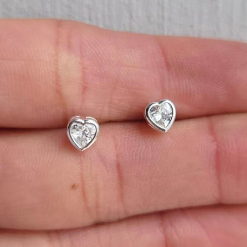 Heart-shaped silver earrings with clear gemstones on a hand.
