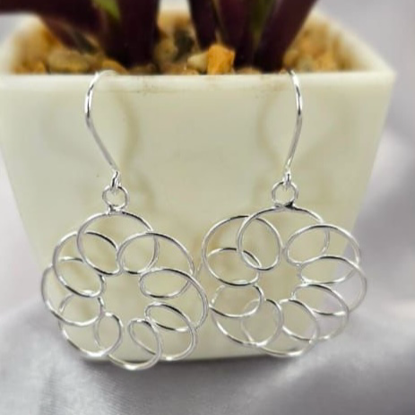 A pair of silver kaleidoscope circle drop earrings displayed in front of a potted plant.