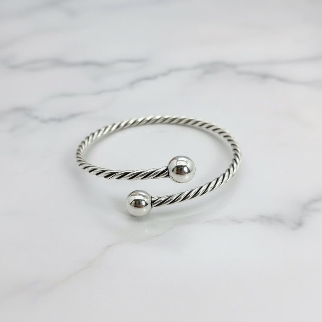 A sterling silver rope ball bangle bracelet worn on a person's wrist, displaying a twisted silver design with two spherical ends.