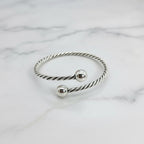 A sterling silver rope ball bangle bracelet worn on a person's wrist, displaying a twisted silver design with two spherical ends.