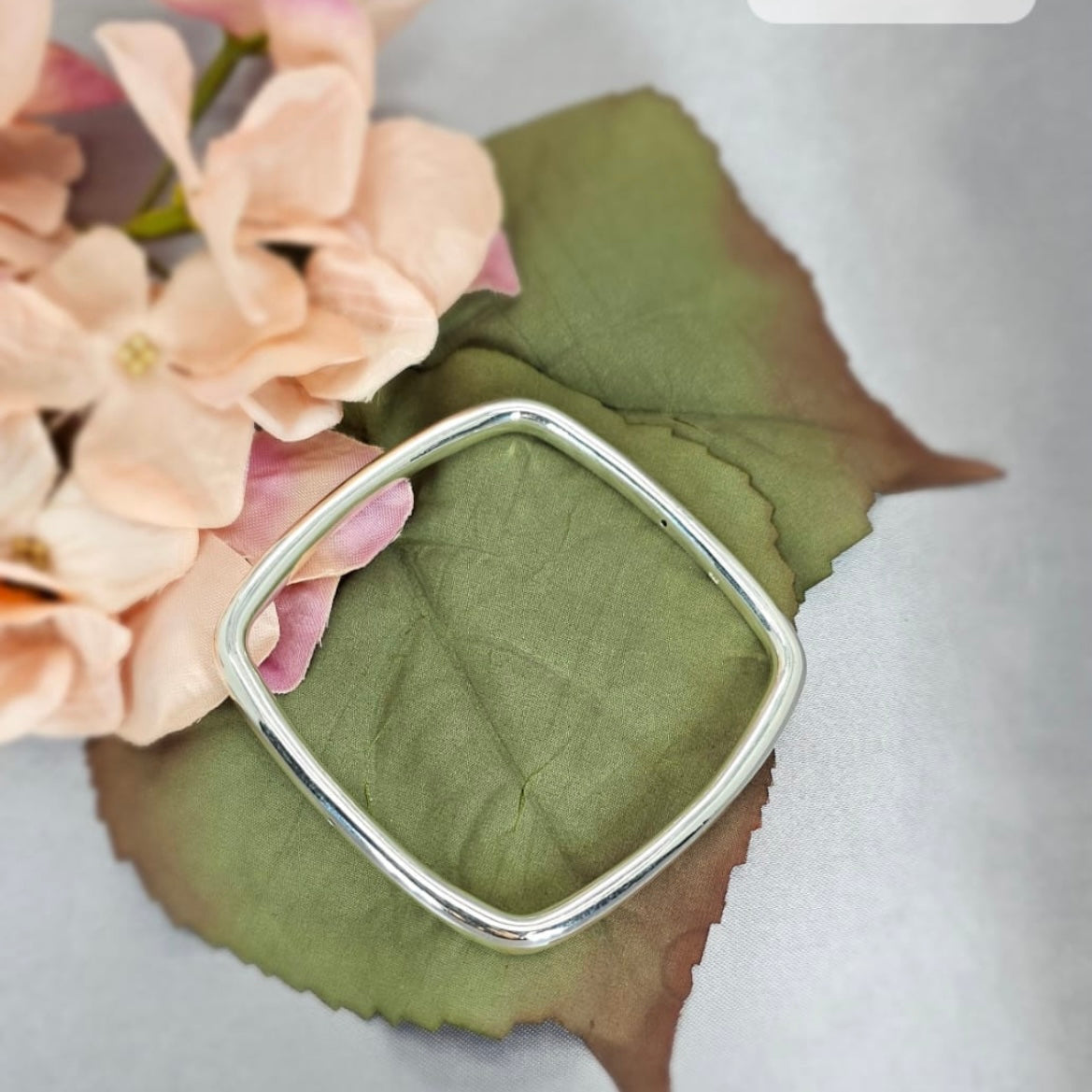 A 6mm square sterling silver bangle bracelet displayed on a green leaf with a pink flower in the background.