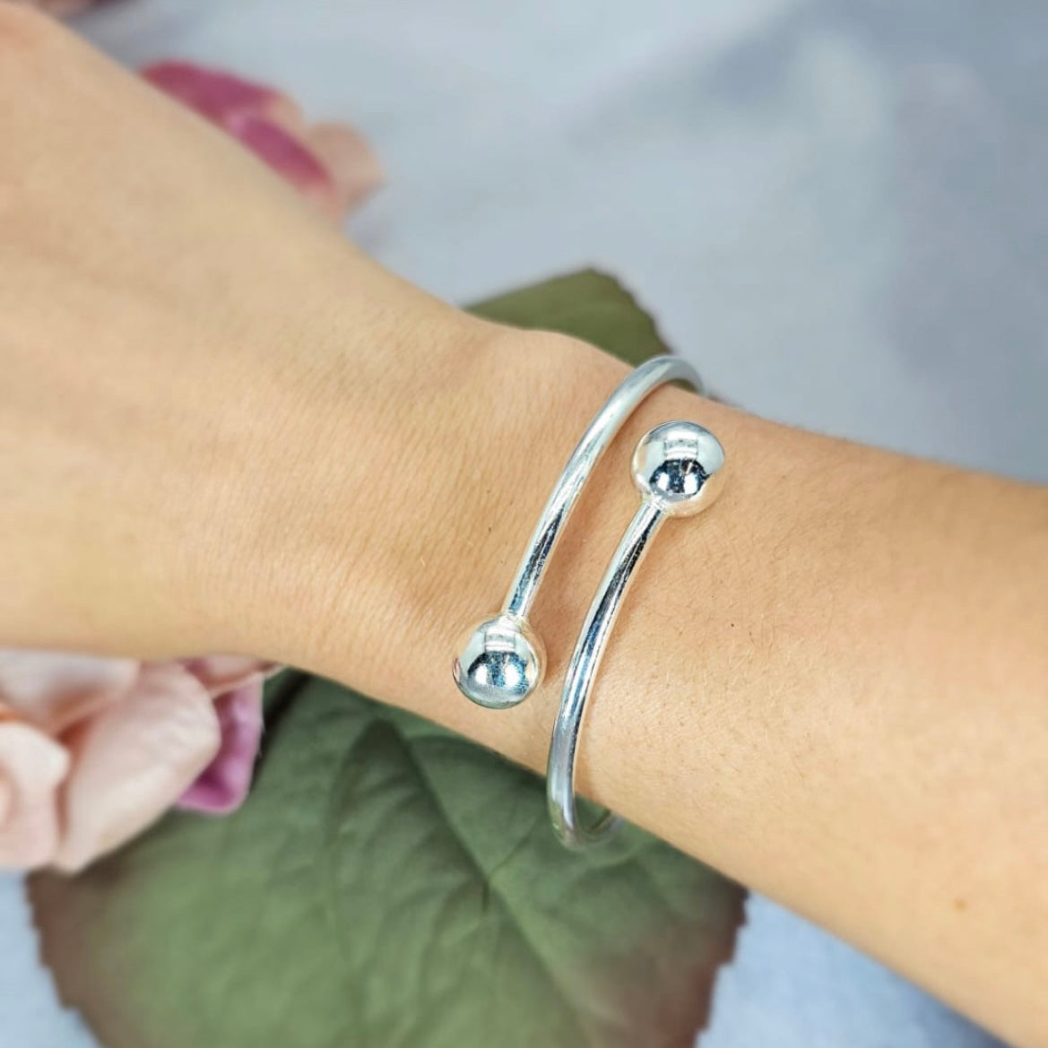 A sterling silver bracelet with a 10mm ball slide closure, displayed on a person's wrist against a floral background.