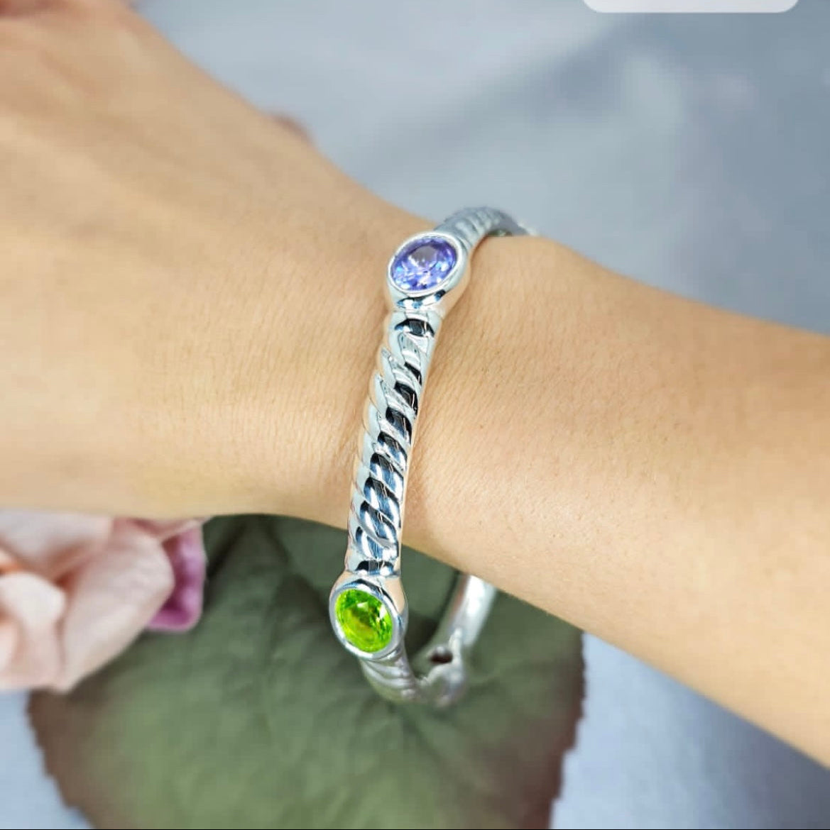 A sterling silver bracelet featuring a bulky design with three colorful stones, displayed on a wrist.