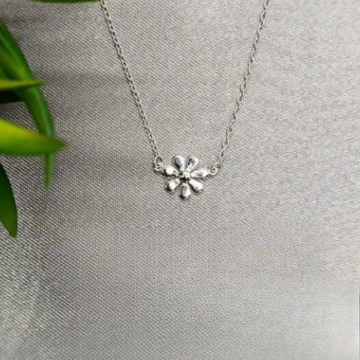 A sterling silver necklace with a daisy pendant, displayed against a grey background with green leaves to the side.
