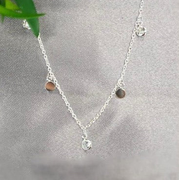 A sterling silver necklace with a delicate disc pendant encrusted with cubic zirconia and small dangling charms, displayed against a grey background.