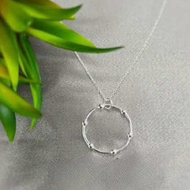 A sterling silver necklace with a detailed circle center, displayed against a textured background with green foliage.