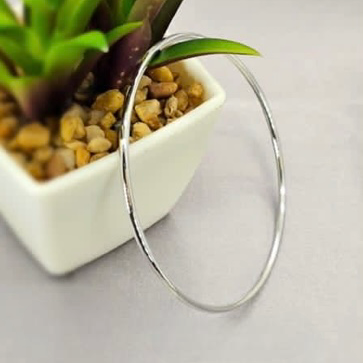 A sterling silver bangle bracelet displayed on a white surface, with a small amount of green plant material in the background.