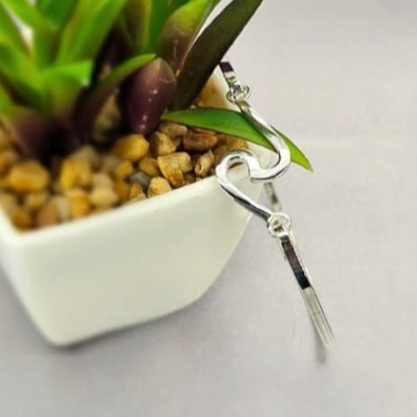 A sterling silver wave bracelet displayed on a white wristband, attached to a small artificial plant in a white vase with pebbles.