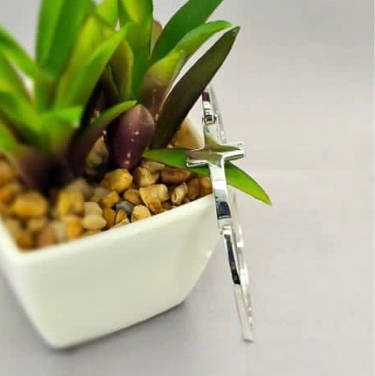 A sterling silver bracelet with a small cross design, displayed on a white surface next to a potted plant.