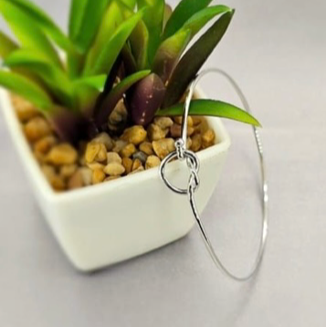 A sterling silver bracelet with a heart-shaped knot displayed on a white surface next to a potted plant.