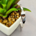 A sterling silver baby bangle bracelet resting on a surface next to a potted plant.