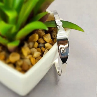 A sterling silver baby bangle bracelet resting on a surface next to a potted plant.