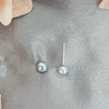 A close-up image of a pair of grey freshwater pearl stud earrings on a textured fabric surface.