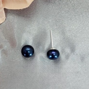 A close-up image of a pair of dark blue freshwater pearl stud earrings on a textured grey background.