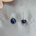 A pair of dark blue freshwater pearl stud earrings set in sterling silver, displayed on a textured grey background.