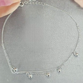 A sterling silver anklet with a double layer design and dangling balls, displayed against a floral background.