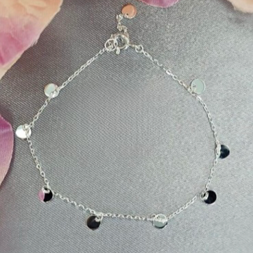A sterling silver bracelet featuring a chain of tiny discs, displayed against a floral background.