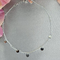A sterling silver bracelet with a series of round beads and two black discs, displayed on a textured background with flowers.